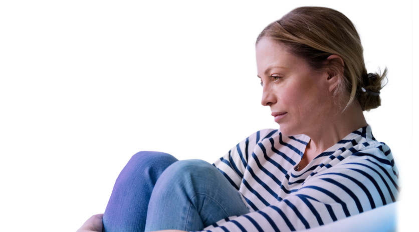 Middle-aged woman sitting with her arms wrapped around her legs, with a blue background.